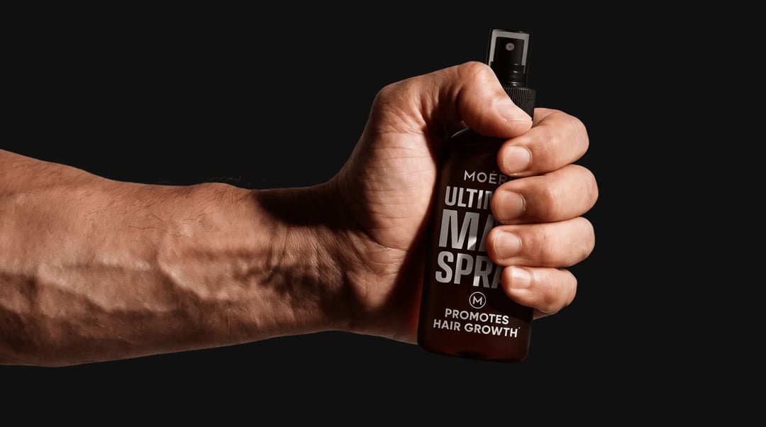 A bottle of Moerie Ultimate Man Spray held in one hand